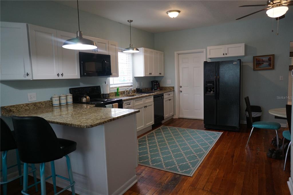 A kitchen with white cabinets, granite countertops, black appliances, and a teal patterned area rug — 601 N OSCEOLA AVENUE, CLEARWATER, FL