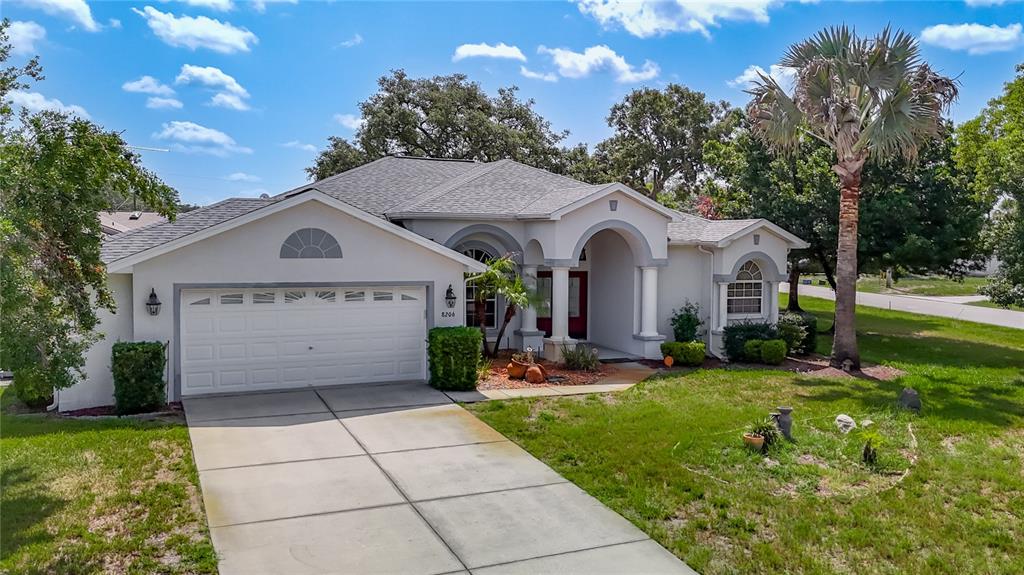 A single-story house with a white stucco exterior, a two-car garage, and a palm tree — 8206 PINEHURST DRIVE, SPRING HILL, FL