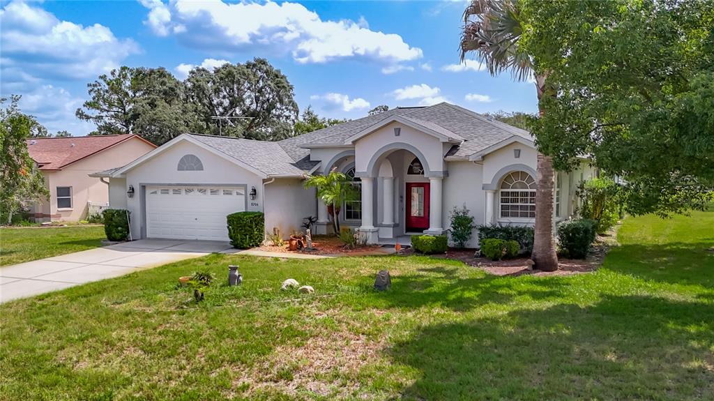 A single-story house with a white stucco exterior, a red front door, and a garage — 8206 PINEHURST DRIVE, SPRING HILL, FL