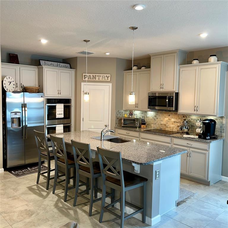 A kitchen features light-colored cabinets, granite countertops, a central island with seating, and stainless appliances — 456 WINTER SOLSTICE LANE, MOUNT DORA, FL