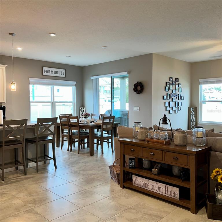 An open-concept dining and living area features tile flooring, farmhouse decor, and neutral walls — 456 WINTER SOLSTICE LANE, MOUNT DORA, FL