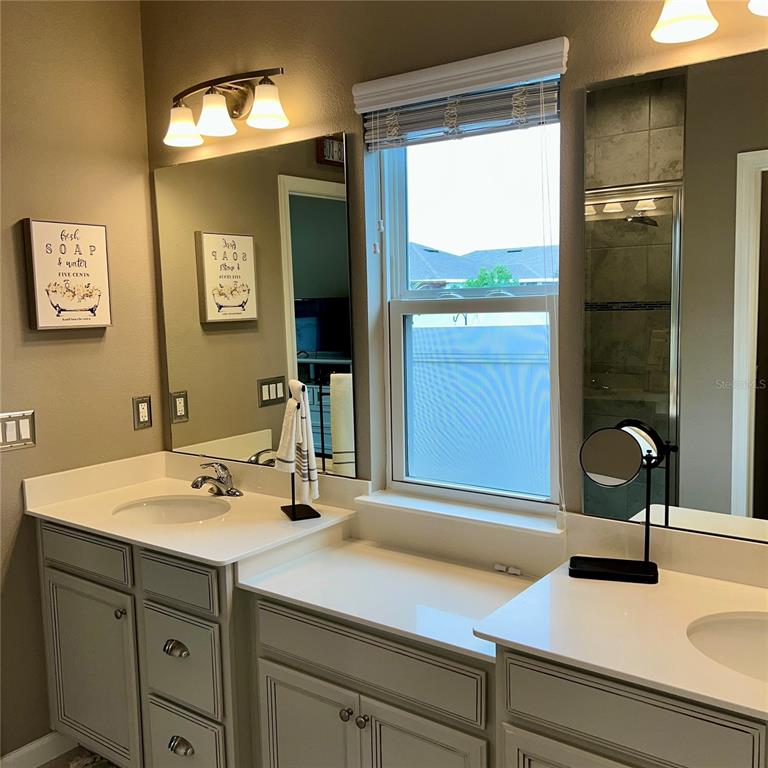 A bathroom features a double vanity with gray cabinets, white countertops, and a window — 456 WINTER SOLSTICE LANE, MOUNT DORA, FL