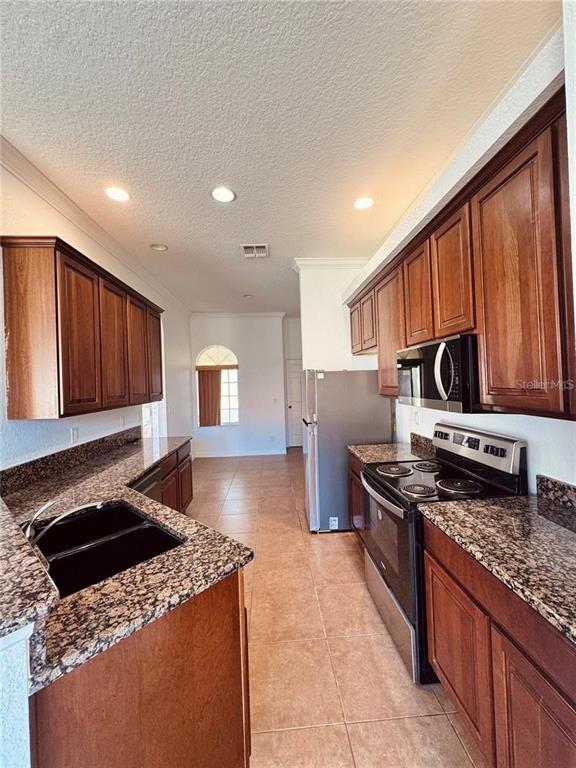 A kitchen features dark wood cabinets, granite countertops, stainless steel appliances, and tile flooring — 449 BAY LEAF DRIVE, POINCIANA, FL