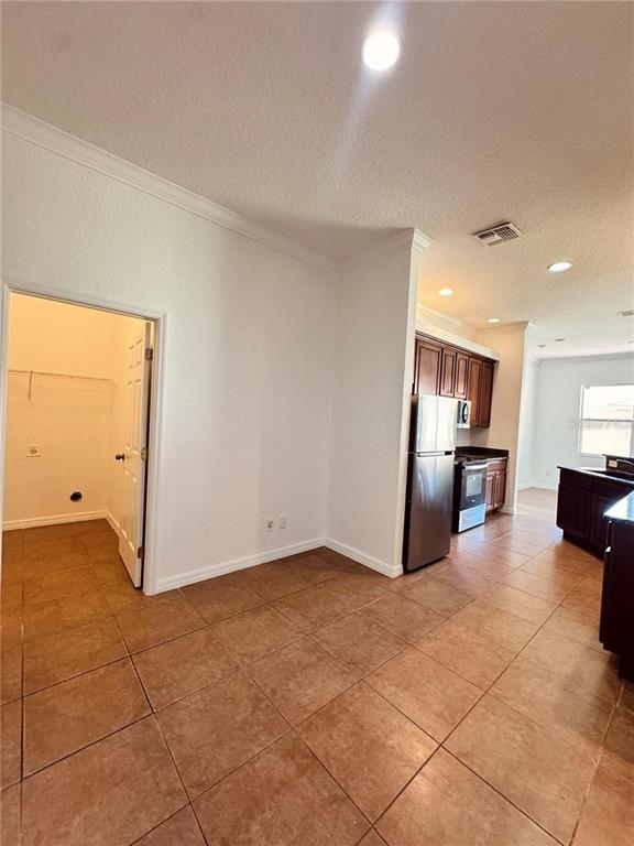 A kitchen with brown cabinets and stainless steel appliances opens to a tiled dining area — 449 BAY LEAF DRIVE, POINCIANA, FL