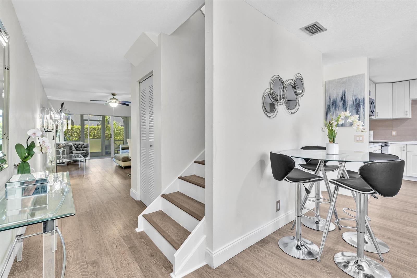 A dining area with a glass table and black stools sits beside a wooden staircase — 6663 Via Regina, Boca Raton FL 33433, BOCA RATON, FL