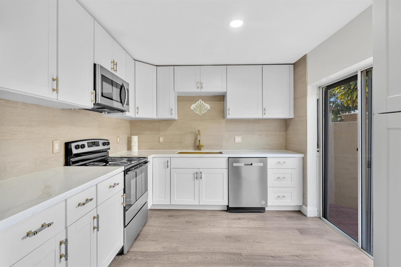 A kitchen with white cabinets, stainless steel appliances, wood-look flooring, and a light-colored backsplash — 6663 Via Regina, Boca Raton FL 33433, BOCA RATON, FL