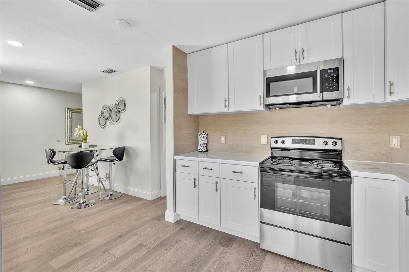 A kitchen with white cabinets, stainless steel appliances, and light wood-look flooring — 6663 Via Regina, Boca Raton FL 33433, BOCA RATON, FL