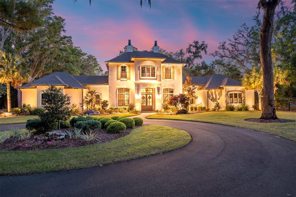 A two-story stucco house with a circular driveway and mature trees at dusk — 14819 NW 21ST AVENUE, NEWBERRY, FL