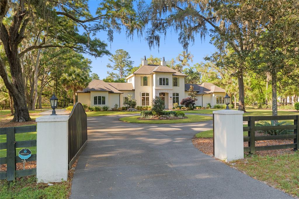 A two-story house with a circular driveway and gated entrance sits among large oak trees — 14819 NW 21ST AVENUE, NEWBERRY, FL