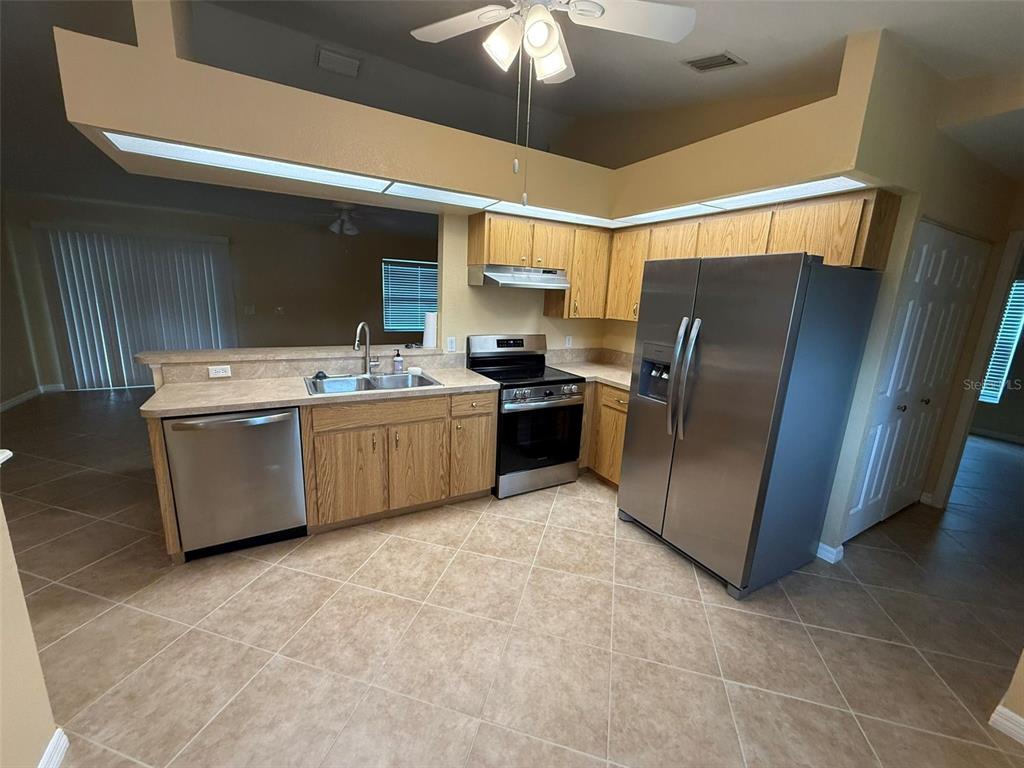A kitchen features light wood cabinets, stainless steel appliances, and beige tile flooring — 7306 TOTEM AVENUE, NORTH PORT, FL
