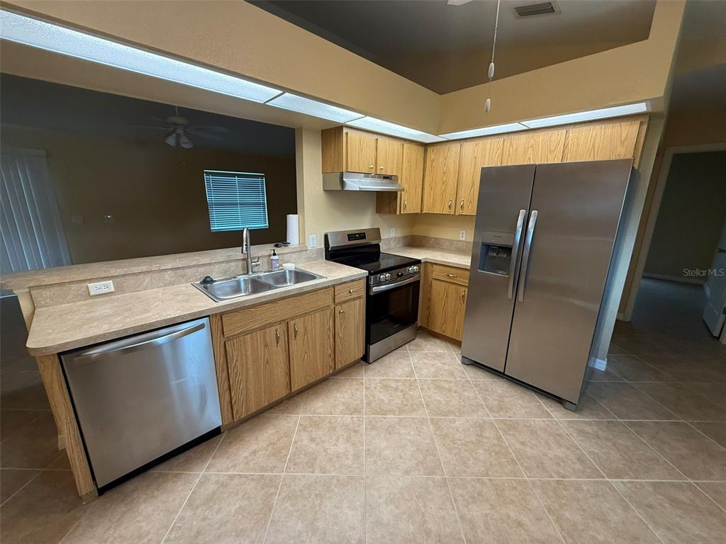 A kitchen features light wood cabinets, stainless steel appliances, and beige tile flooring — 7306 TOTEM AVENUE, NORTH PORT, FL