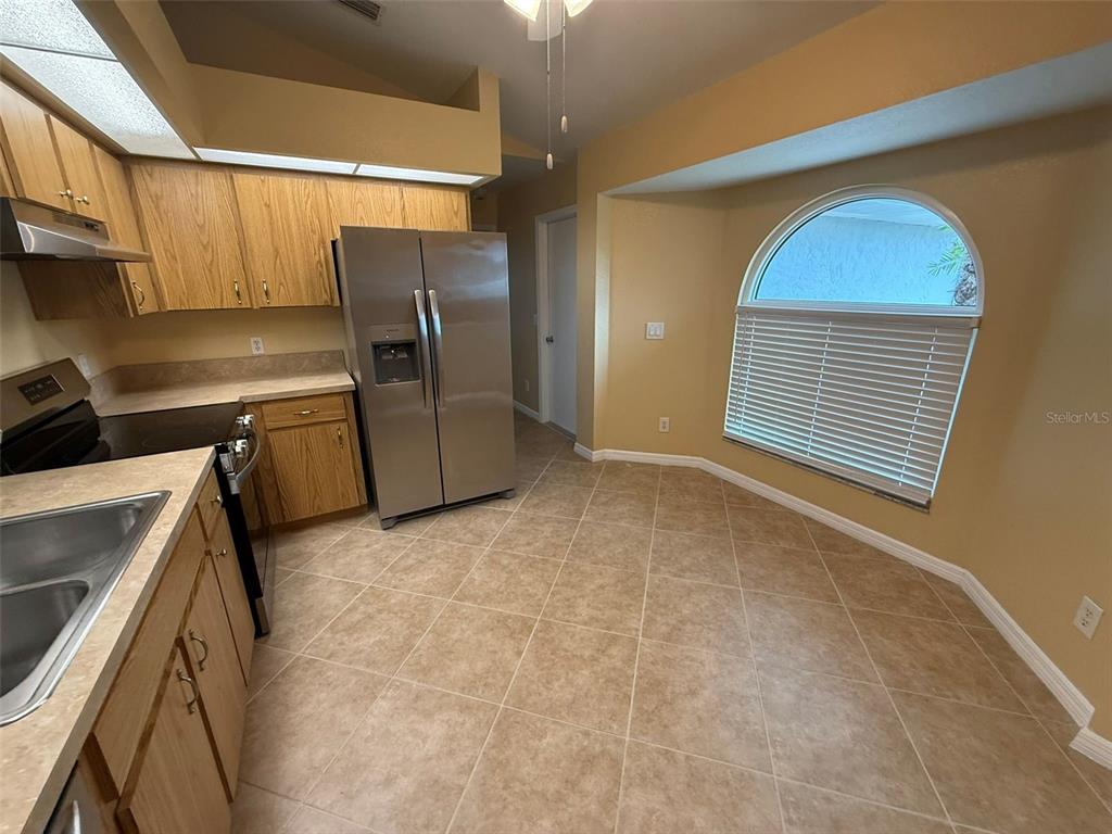 A kitchen features light wood cabinets, stainless steel appliances, tile flooring, and a large window — 7306 TOTEM AVENUE, NORTH PORT, FL