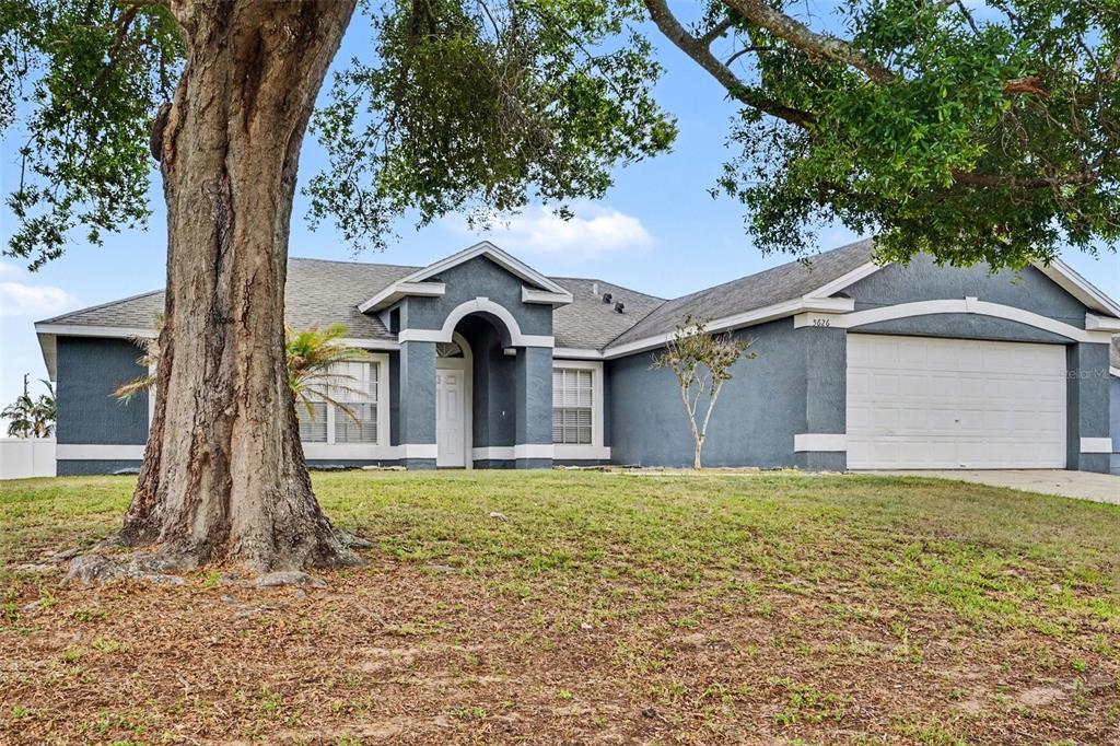 A single-story blue house with a white garage door and a large tree in front — 5626 S LOMA VISTA COURT, DAVENPORT, FL