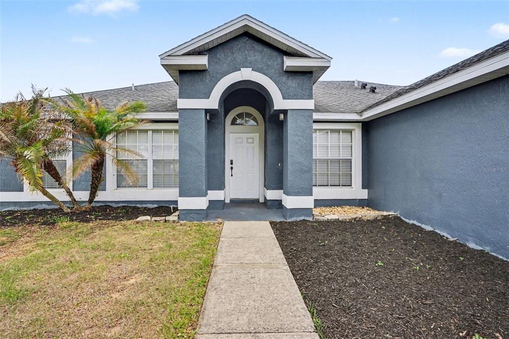 A dark gray house exterior features a white arched entryway and a concrete walkway — 5626 S LOMA VISTA COURT, DAVENPORT, FL