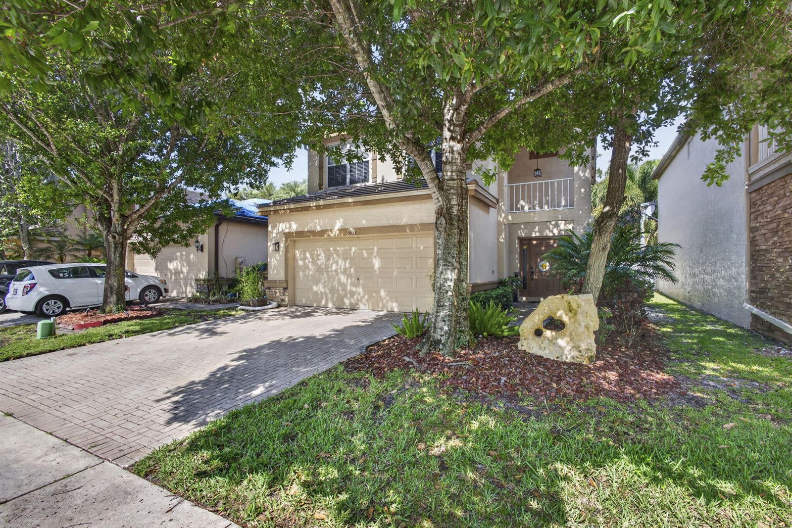 A two-story house with a beige stucco exterior, a paved driveway, and a large tree — 5953 Asturian Trail, Lake Worth FL 33449, LAKE WORTH, FL