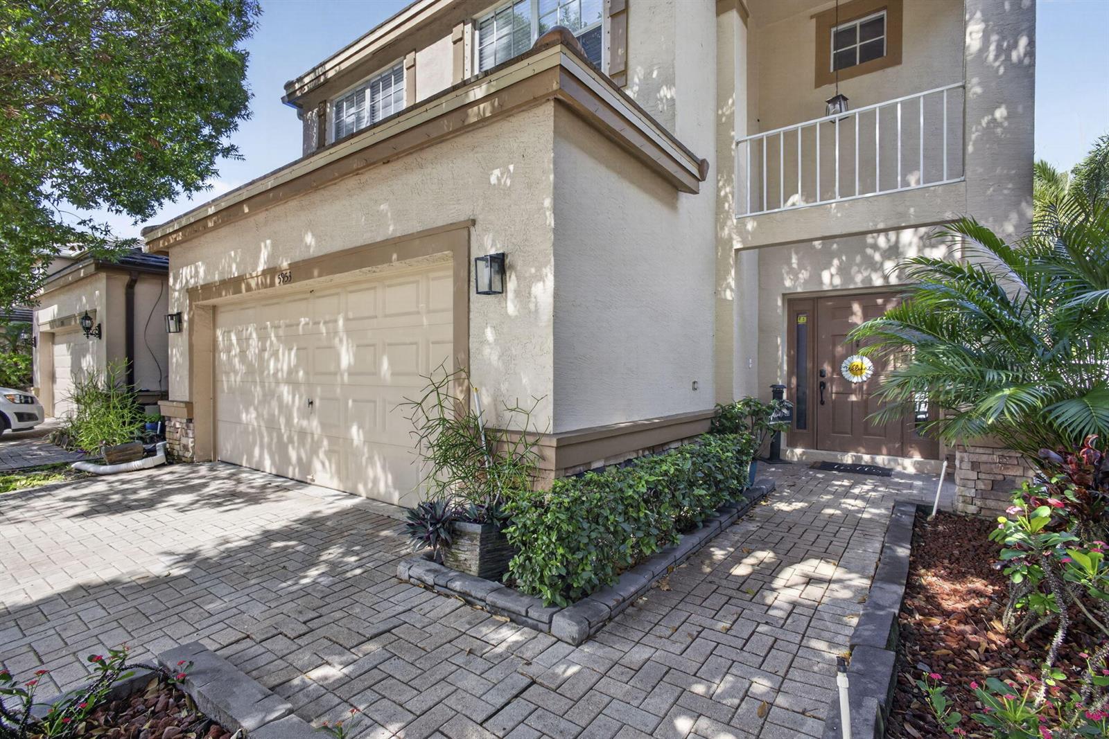 A two-story house exterior features a beige stucco facade, a garage, and a paved walkway — 5953 Asturian Trail, Lake Worth FL 33449, LAKE WORTH, FL