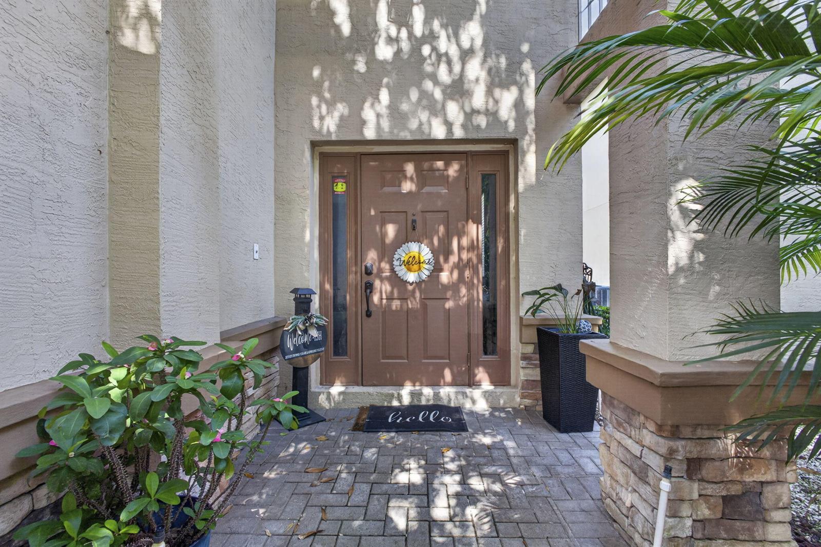 A front entryway features a brown door, a welcome mat, and potted plants on pavers — 5953 Asturian Trail, Lake Worth FL 33449, LAKE WORTH, FL