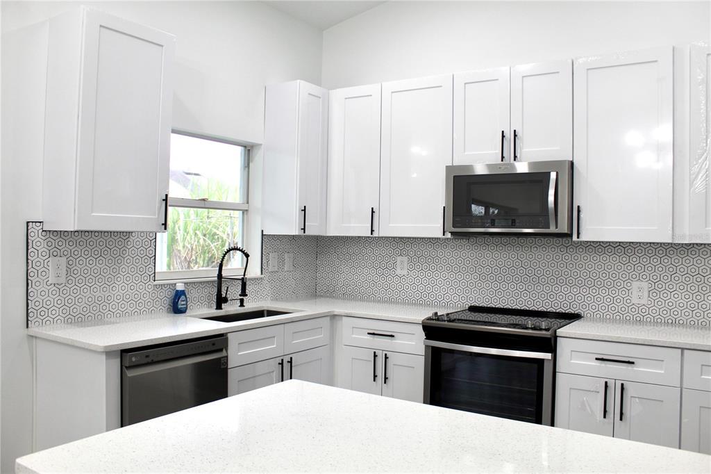 A modern kitchen features white shaker cabinets, stainless steel appliances, and a geometric patterned backsplash — 602 CHEETAH LANE, KISSIMMEE, FL