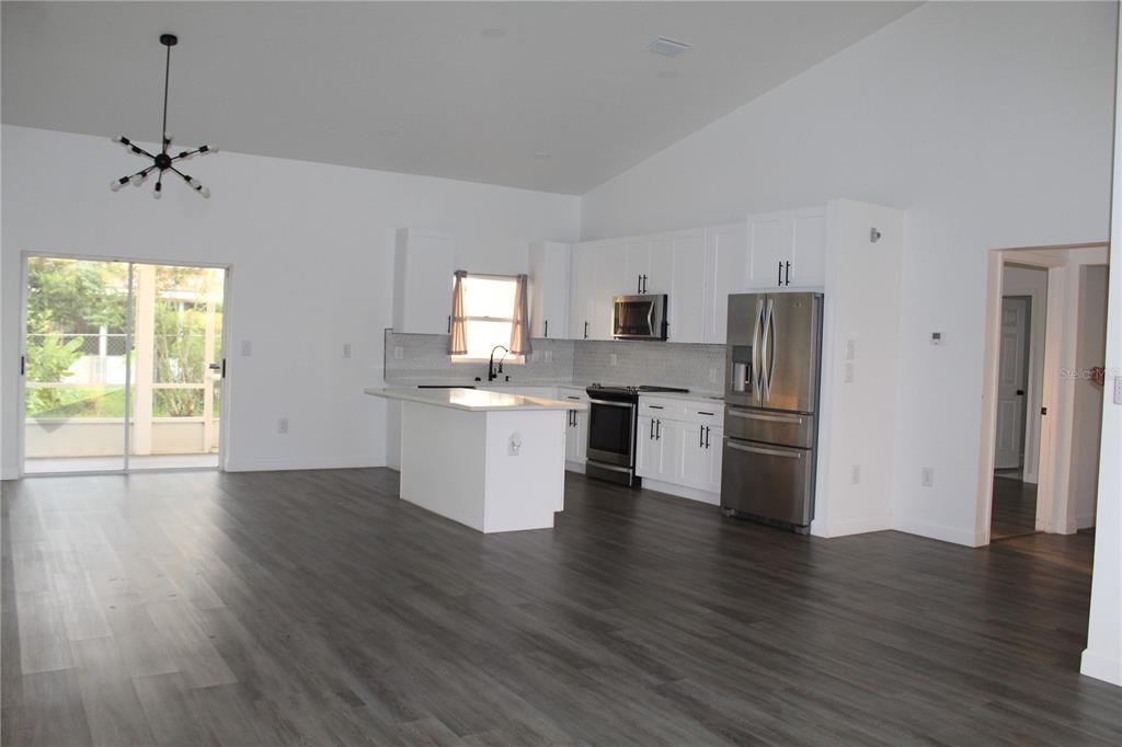 A kitchen with white cabinets, stainless steel appliances, and an island opens to a living area — 602 CHEETAH LANE, KISSIMMEE, FL