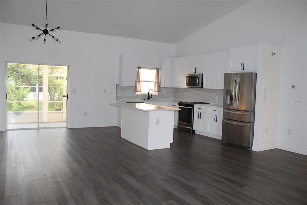 A modern kitchen with white cabinets, stainless steel appliances, and an island, open to a living area — 602 CHEETAH LANE, KISSIMMEE, FL