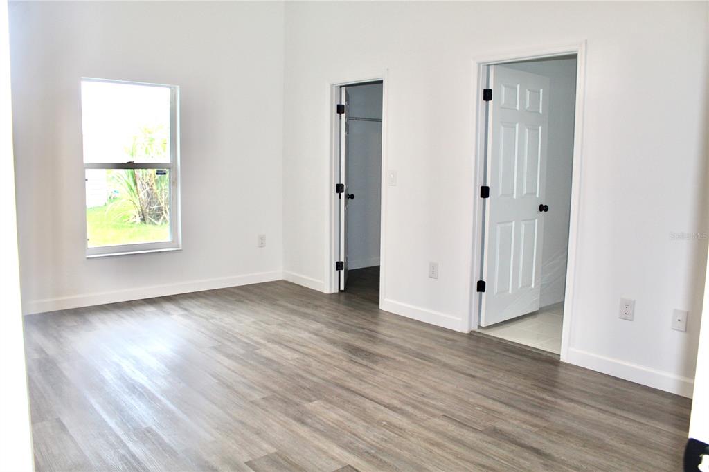A bedroom with light wood-look flooring, white walls, a window, and two open doorways — 602 CHEETAH LANE, KISSIMMEE, FL