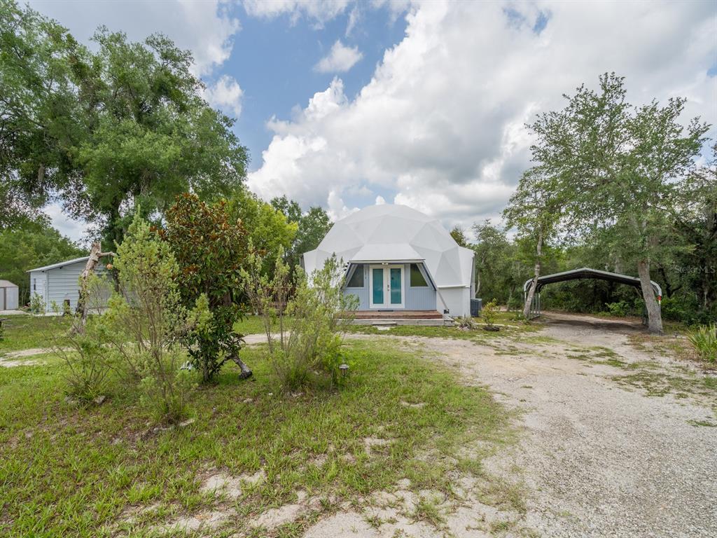 A white geodesic dome house stands on a gravel lot with trees and a carport — 30810 NE 78 STREET, FORT MC COY, FL
