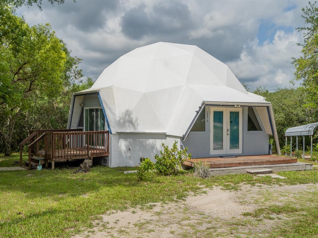 A white geodesic dome house features a wooden deck and a front entrance with double doors — 30810 NE 78 STREET, FORT MC COY, FL