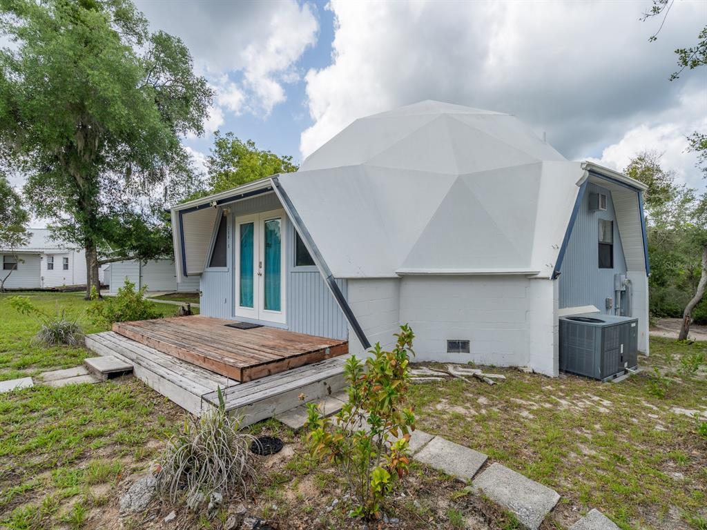 A white geodesic dome house features a wooden deck and blue trim in a grassy yard — 30810 NE 78 STREET, FORT MC COY, FL