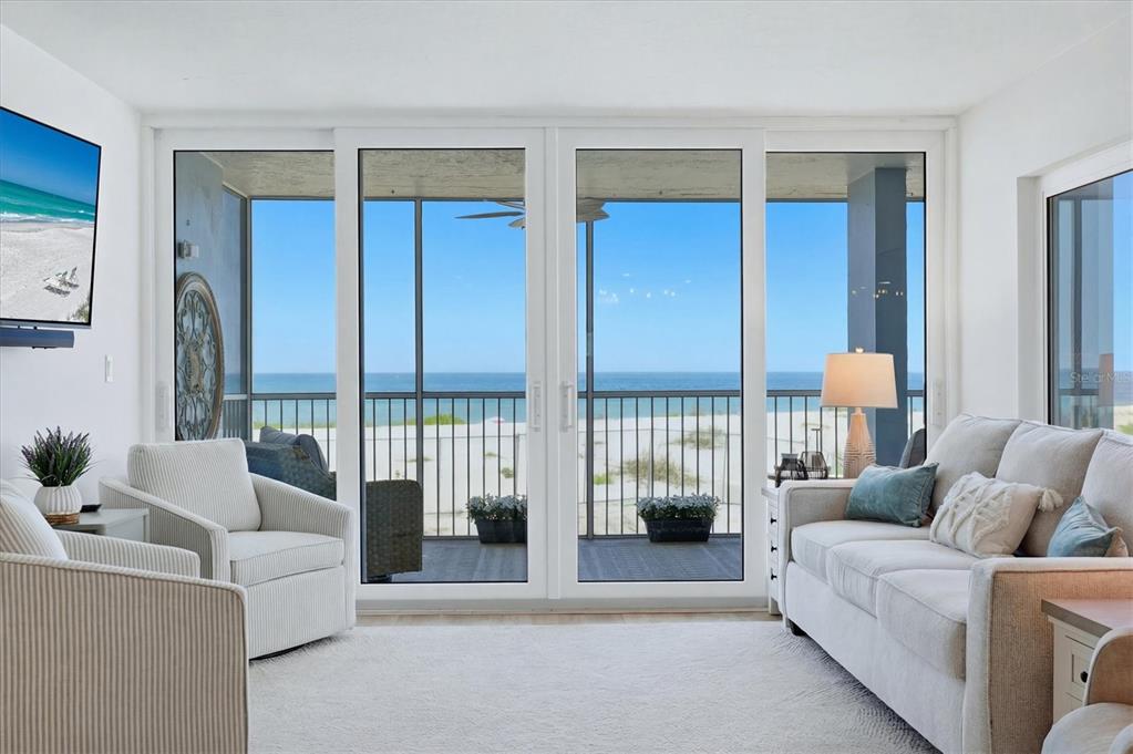 A living room with white furniture faces a balcony overlooking the beach and ocean — 555 THE ESPLANADE N UNIT 205, VENICE, FL
