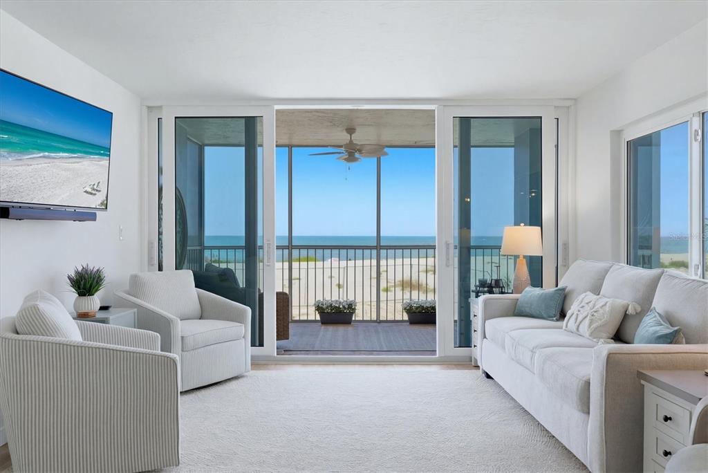 A bright living room features white furniture, a television, and sliding doors opening to a balcony — 555 THE ESPLANADE N UNIT 205, VENICE, FL