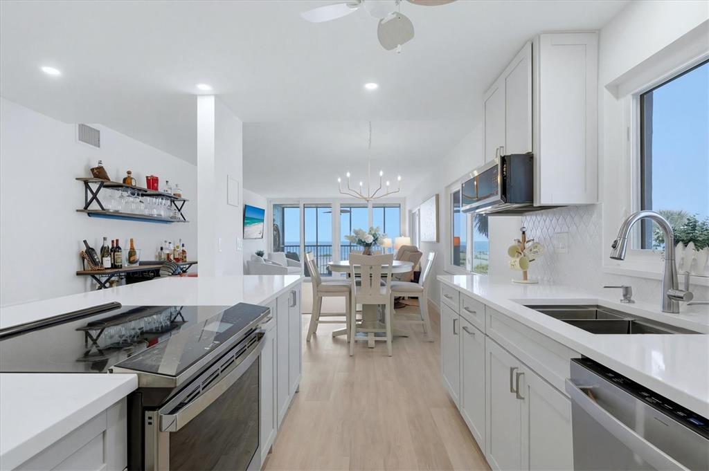 A bright kitchen with white cabinets and quartz countertops overlooks a dining area and ocean — 555 THE ESPLANADE N UNIT 205, VENICE, FL