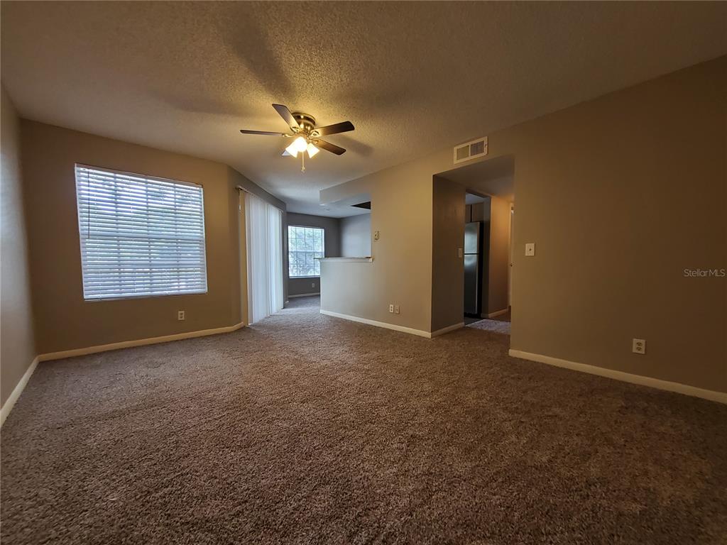 A carpeted living room features a ceiling fan, beige walls, and a sliding glass door — 11526 WESTWOOD BOULEVARD UNIT 725, ORLANDO, FL