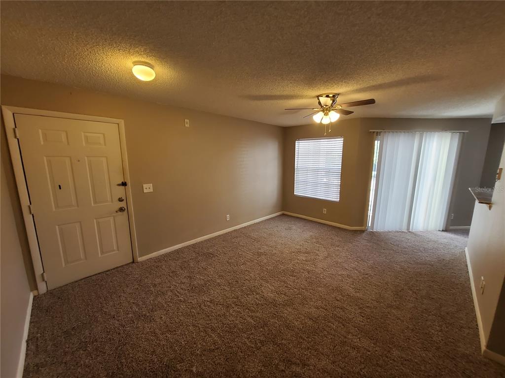 An empty living room features beige walls, brown carpet, a ceiling fan, and a sliding door — 11526 WESTWOOD BOULEVARD UNIT 725, ORLANDO, FL