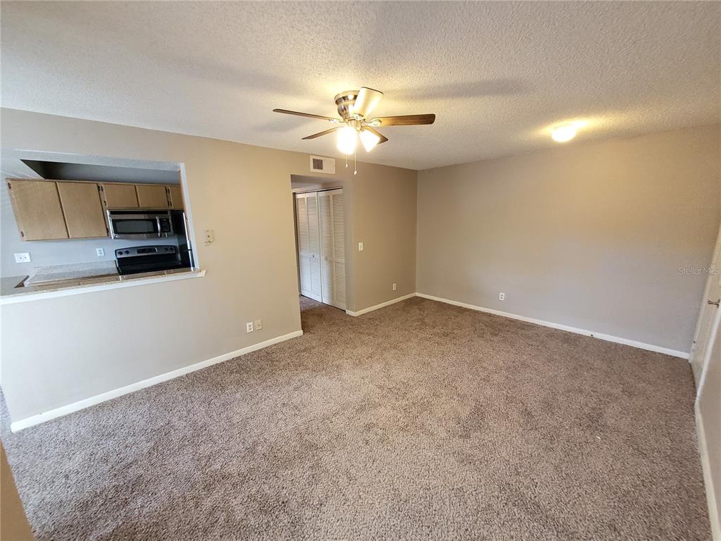 An interior view shows a carpeted living room with a ceiling fan and kitchen pass-through — 11526 WESTWOOD BOULEVARD UNIT 725, ORLANDO, FL
