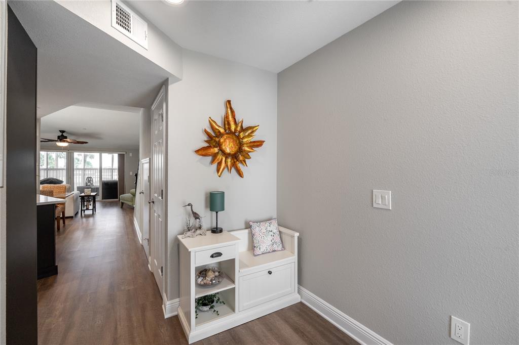A white entryway bench sits against a gray wall beneath a decorative sun wall hanging — 2255 N BEACH ROAD UNIT 12, ENGLEWOOD, FL