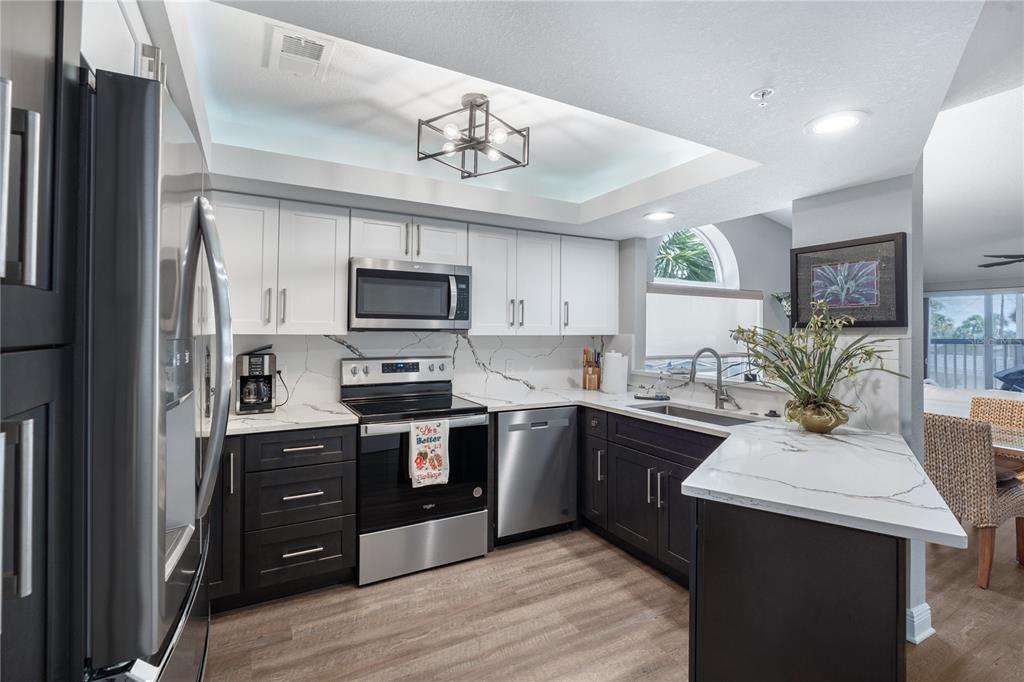 A kitchen features white upper cabinets, dark lower cabinets, stainless steel appliances, and marble countertops — 2255 N BEACH ROAD UNIT 12, ENGLEWOOD, FL