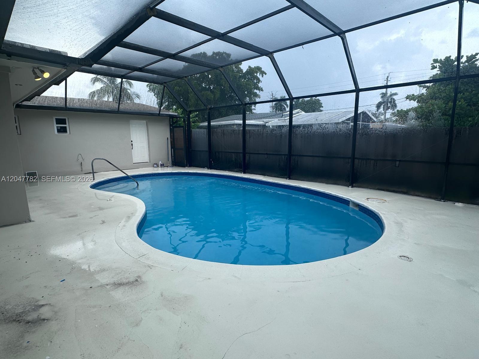 A kidney-shaped swimming pool sits on a concrete patio enclosed by a screened-in lanai — 4380 SW 49th Ct # 0, Dania Beach FL 33314, DANIA BEACH, FL