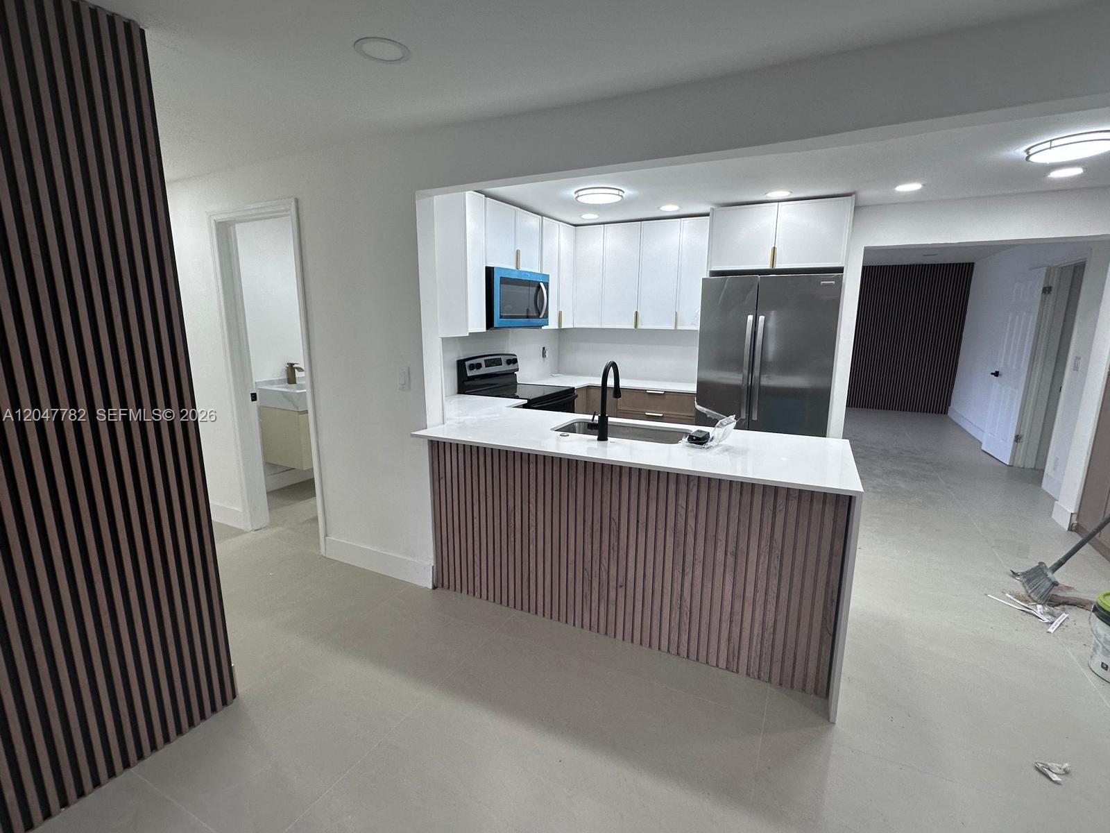 A kitchen features white cabinets, stainless steel appliances, and a wood-slatted peninsula island — 4380 SW 49th Ct # 0, Dania Beach FL 33314, DANIA BEACH, FL