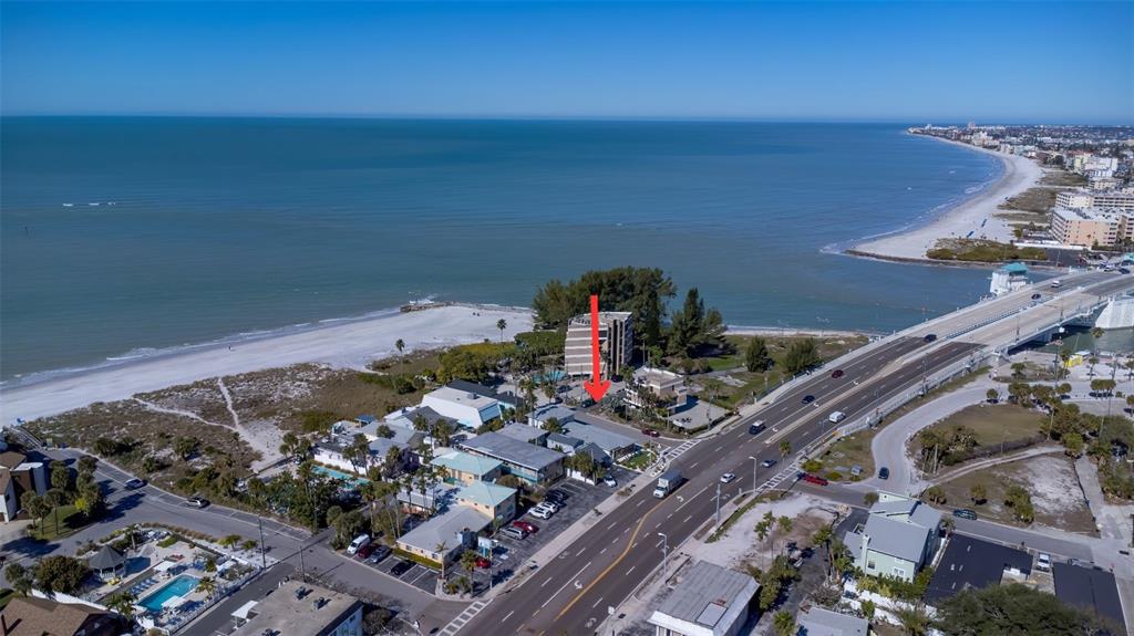 An aerial view shows a coastal area with a beach, a bridge, and a red arrow — 12620 GULF BOULEVARD, TREASURE ISLAND, FL