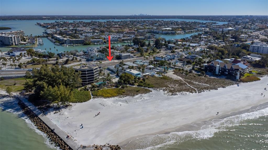 An aerial view shows a sandy beach, coastal buildings, and a jetty on a sunny day — 12620 GULF BOULEVARD, TREASURE ISLAND, FL