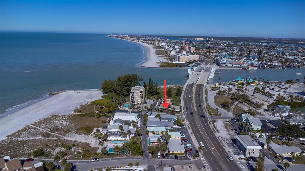 An aerial view shows a coastal area with a beach, a bridge, and buildings — 12620 GULF BOULEVARD, TREASURE ISLAND, FL