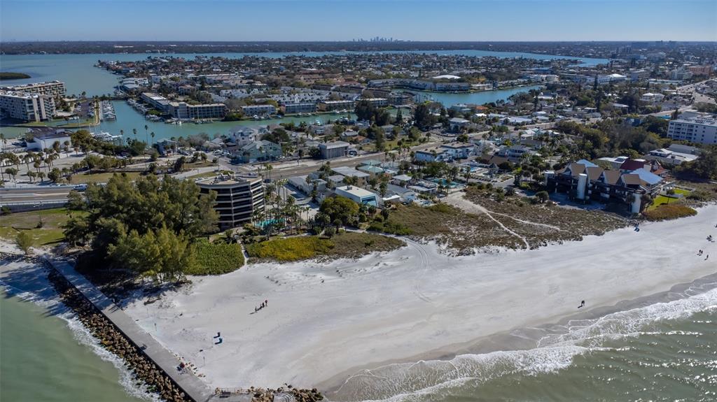 An aerial view shows a sandy beach, a jetty, and nearby multi-story residential buildings — 12620 GULF BOULEVARD, TREASURE ISLAND, FL