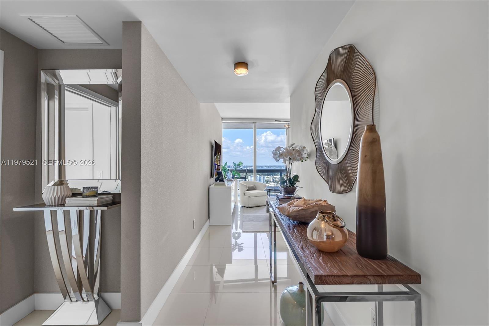 A bright hallway features a console table, a decorative mirror, and a view of the ocean — 6899 Collins Ave # 2403, Miami Beach FL 33141, MIAMI BEACH, FL