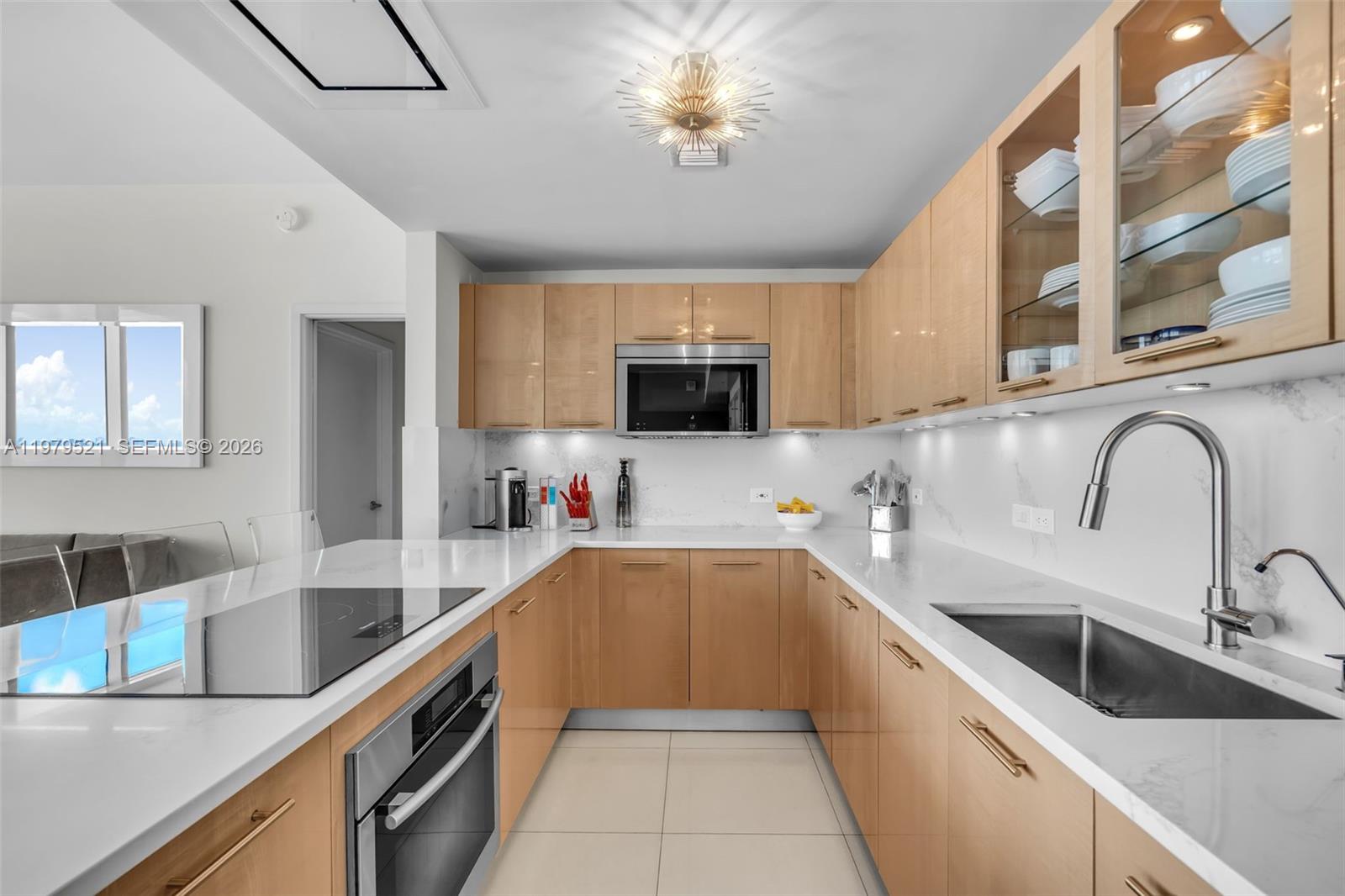 A modern kitchen features light wood cabinets, white countertops, stainless steel appliances, and tile flooring — 6899 Collins Ave # 2403, Miami Beach FL 33141, MIAMI BEACH, FL
