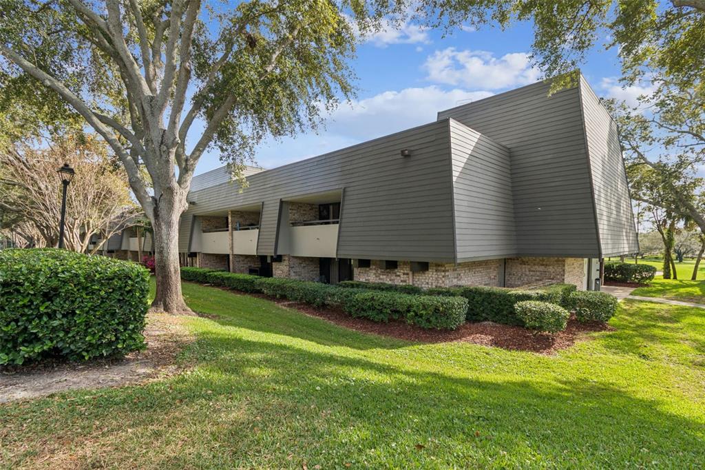 A multi-story apartment building with horizontal siding and balconies sits on a grassy lawn — 36750 US HIGHWAY 19 N UNIT 13207, PALM HARBOR, FL