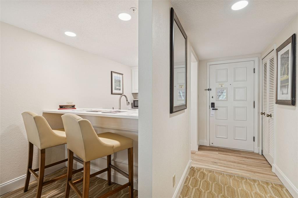 A view of a kitchen breakfast bar with two stools next to an entryway door — 36750 US HIGHWAY 19 N UNIT 13207, PALM HARBOR, FL