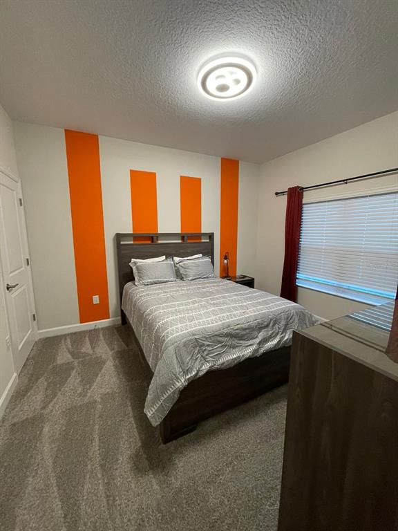 A bedroom features a bed with a grey patterned comforter against a wall with orange stripes — 1144 CHALLENGE DRIVE, DAVENPORT, FL