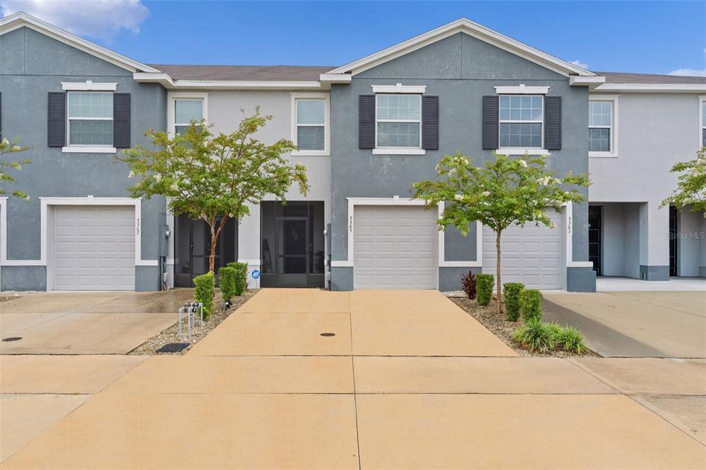 A row of multi-story townhouses features gray stucco facades, attached garages, and small front trees — 5365 PINECONE COURT, WILDWOOD, FL