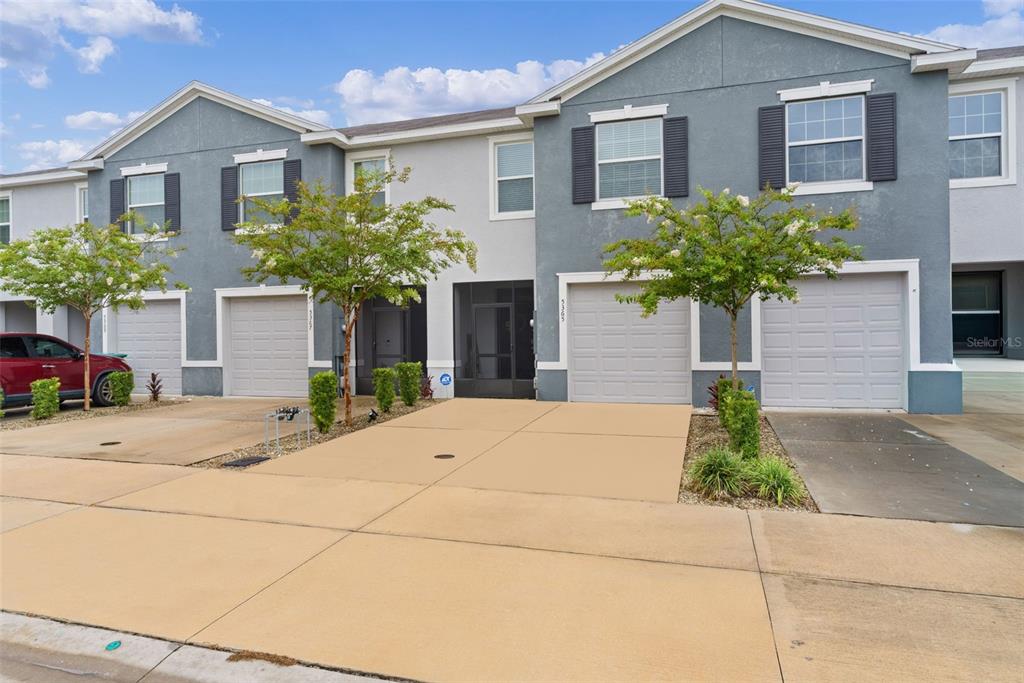 The exterior of two adjacent townhomes features gray siding, attached garages, and small front trees — 5365 PINECONE COURT, WILDWOOD, FL
