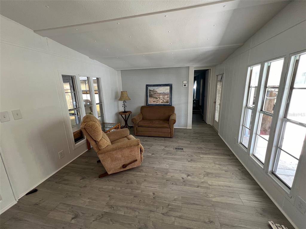 A living room with light gray wood-look flooring, white walls, and several large windows — 11 SHADY LANE, PALMETTO, FL